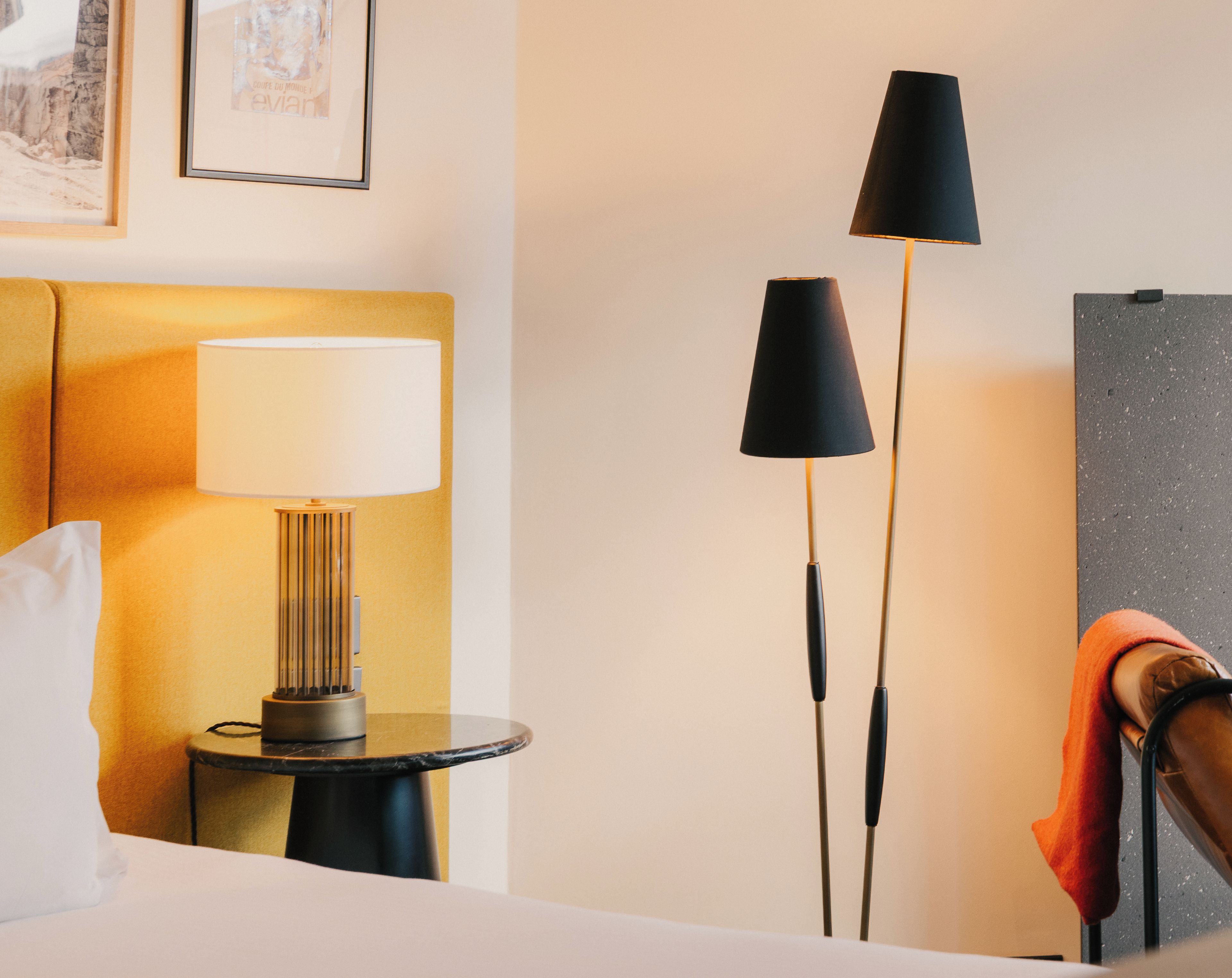 Une chambre d’hôtel avec un lit, une lampe de chevet, une lampe sur pied et un tableau encadré au mur.