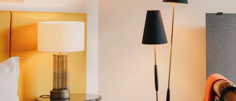 A hotel room with a bed, a bedside lamp, a floor lamp, and a framed picture on the wall.