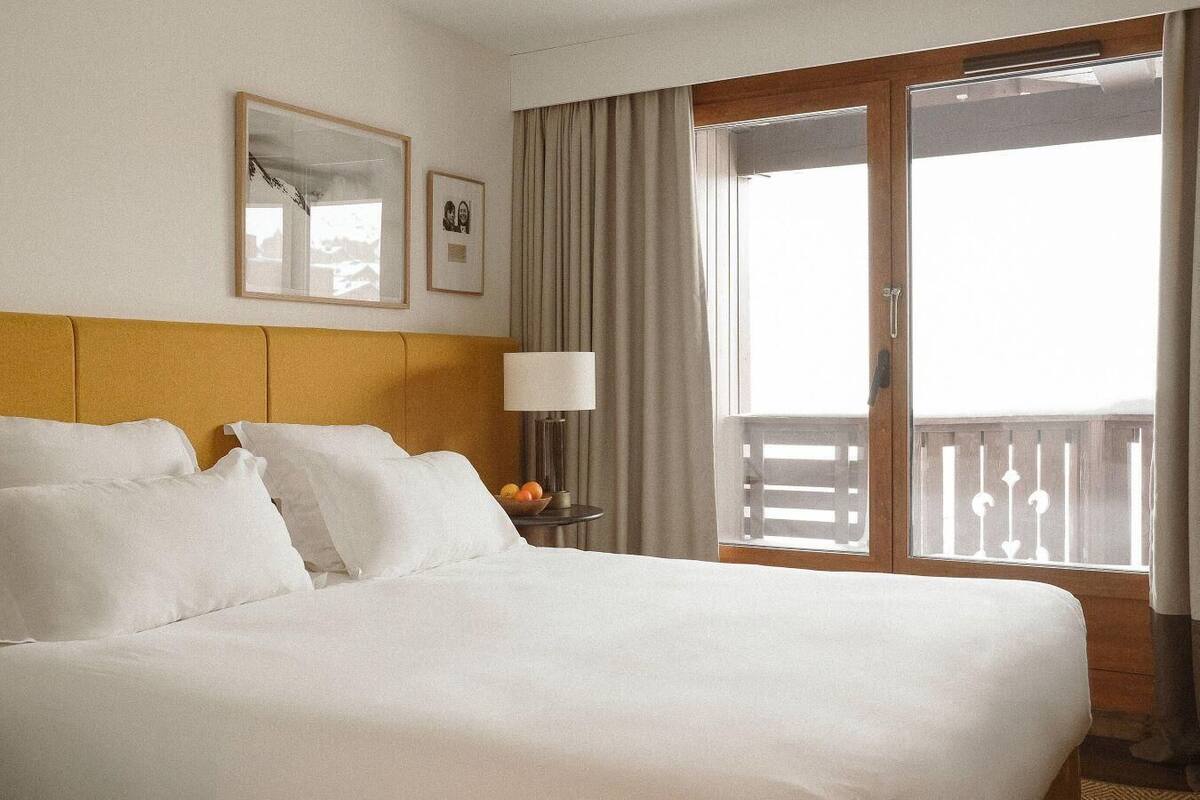 A hotel room with a bed, a nightstand with a lamp, a framed picture, and a window with curtains.