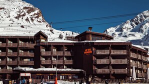 A multi-story wooden building with balconies, a sign reading 'Le Val Thorens,' and a snowy mountain backdrop. - Le Val Thorens (Les Belleville)