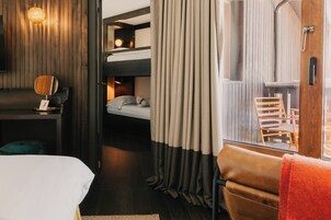 Habitación de hotel con literas, un escritorio con lámpara, una silla y una ventana con cortinas.