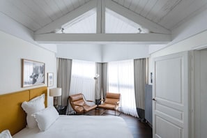 Una habitación de hotel con una cama, dos sillones de cuero, un escritorio, una lámpara y un ventanal con cortinas.