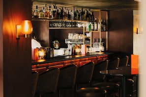 Zona de bar con estanterías llenas de botellas, una barra y varias sillas.