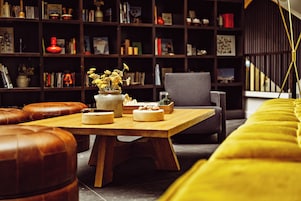 Un espacio de sala acogedor con una mesa de centro de madera, otomanas de cuero, una estantería y un sofá amarillo.