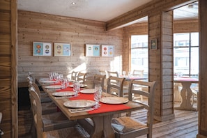 A wooden interior with a long dining table set for a meal, wooden walls, and framed pictures on the wall. - Le Val Thorens (Les Belleville)