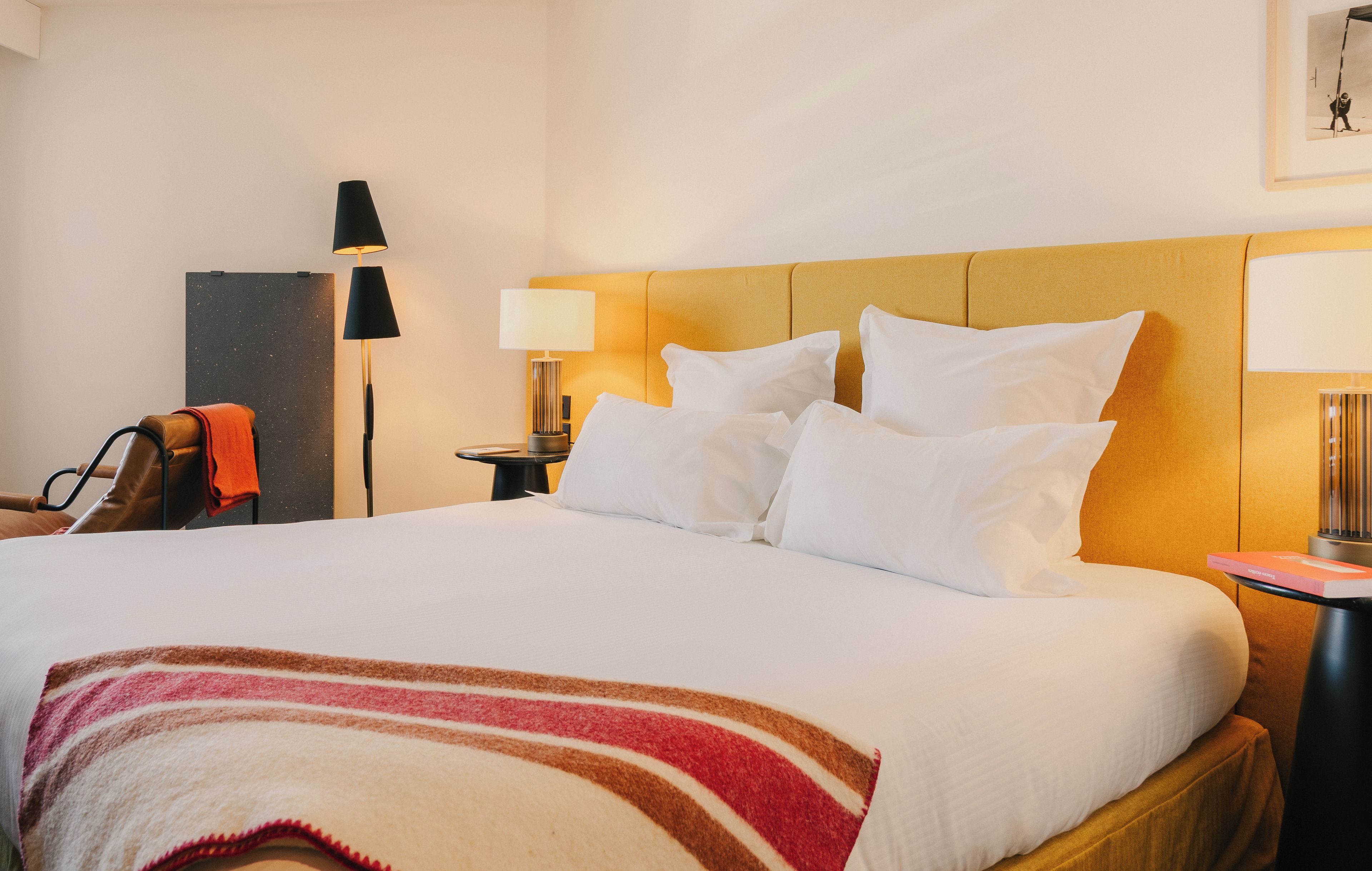Habitación de hotel con una cama, una mesita de noche, una lámpara, una silla y un cuadro colgado en la pared.
