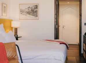 A hotel room with a bed, a nightstand with a lamp, a door, and a wall-mounted picture.
