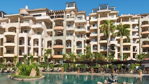 Un hôtel doté de nombreux balcons, d’une piscine avec des chaises longues et de palmiers.