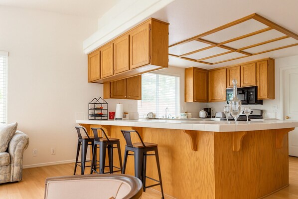 Una cocina moderna con armarios de madera, una isla central con taburetes de bar y un microondas integrado.