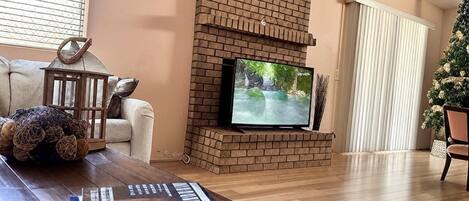 A living room with a brick fireplace, a television, a coffee table with books, and a Christmas tree.