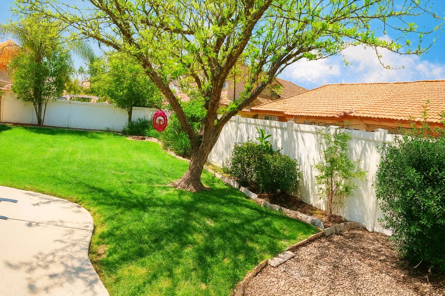 Una propiedad residencial con un césped cuidado, un árbol y una cerca blanca.