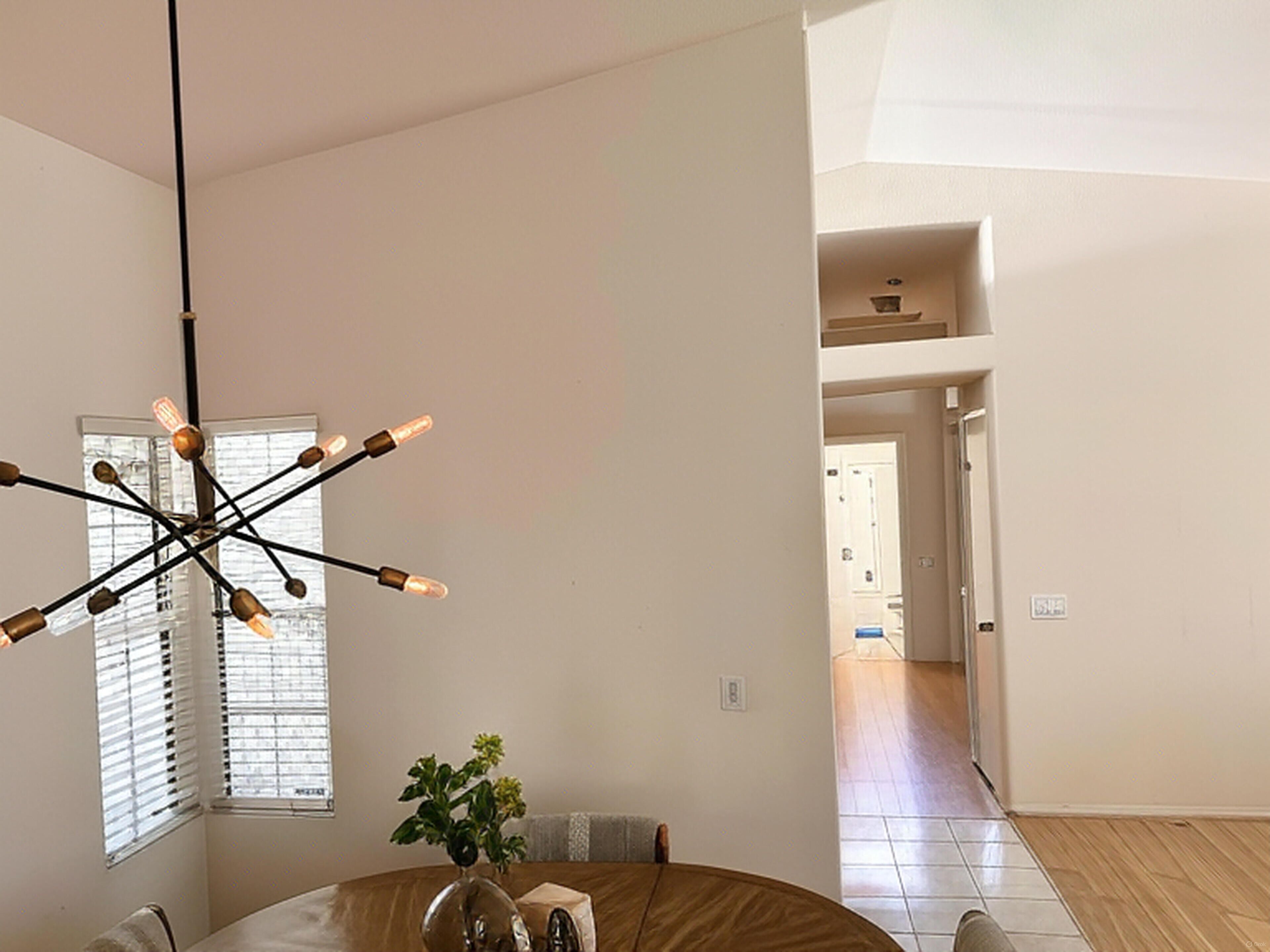 A spacious room with a modern chandelier, a dining table with chairs, and a view of a hallway leading to another room.