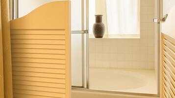 A bathroom with a glass shower enclosure, a bathtub, and a window with a curtain.