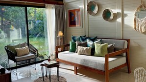 A spacious room with a large window, a ceiling fan, a wooden sofa, a chair, and a small table.