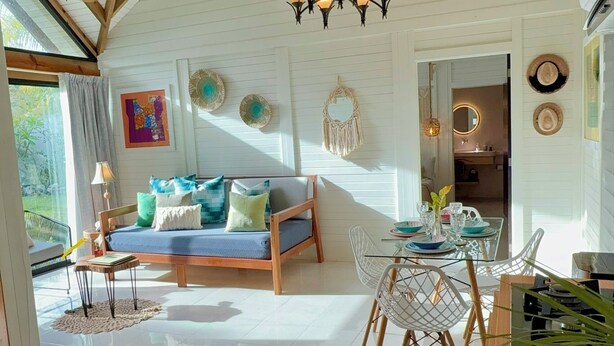 A spacious room with a high ceiling, a chandelier, a sofa, a dining table with chairs, and a kitchen area.