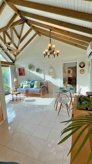 Um quarto espaçoso com pé direito alto, um candelabro, um sofá, uma mesa de jantar com cadeiras e uma área de cozinha.