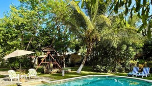 A swimming pool surrounded by grass, palm trees, and a wooden structure.