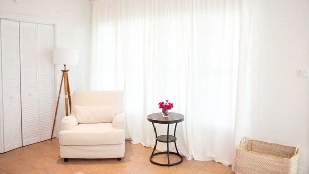 Une pièce avec un canapé blanc, une petite table ronde ornée d’un vase de fleurs, un lampadaire sur trépied et un panier en osier.