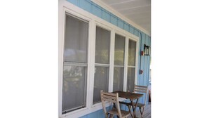 Une véranda avec une table et des chaises, de grandes fenêtres et un mur extérieur bleu.
