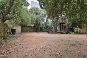 A backyard with a dirt path, a wooden fence, and a house with a staircase leading to a porch.