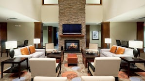 Un hall de hotel con chimenea, sofás, sillones y una alfombra estampada.