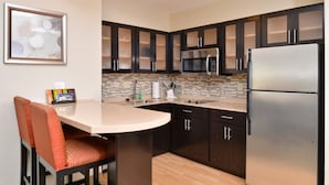 Una cocina moderna con armarios oscuros, un refrigerador de acero inoxidable, un microondas y un taburete de bar.