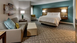Habitación de hotel con cama, sofá, mesita auxiliar, lámpara y obras de arte en la pared.