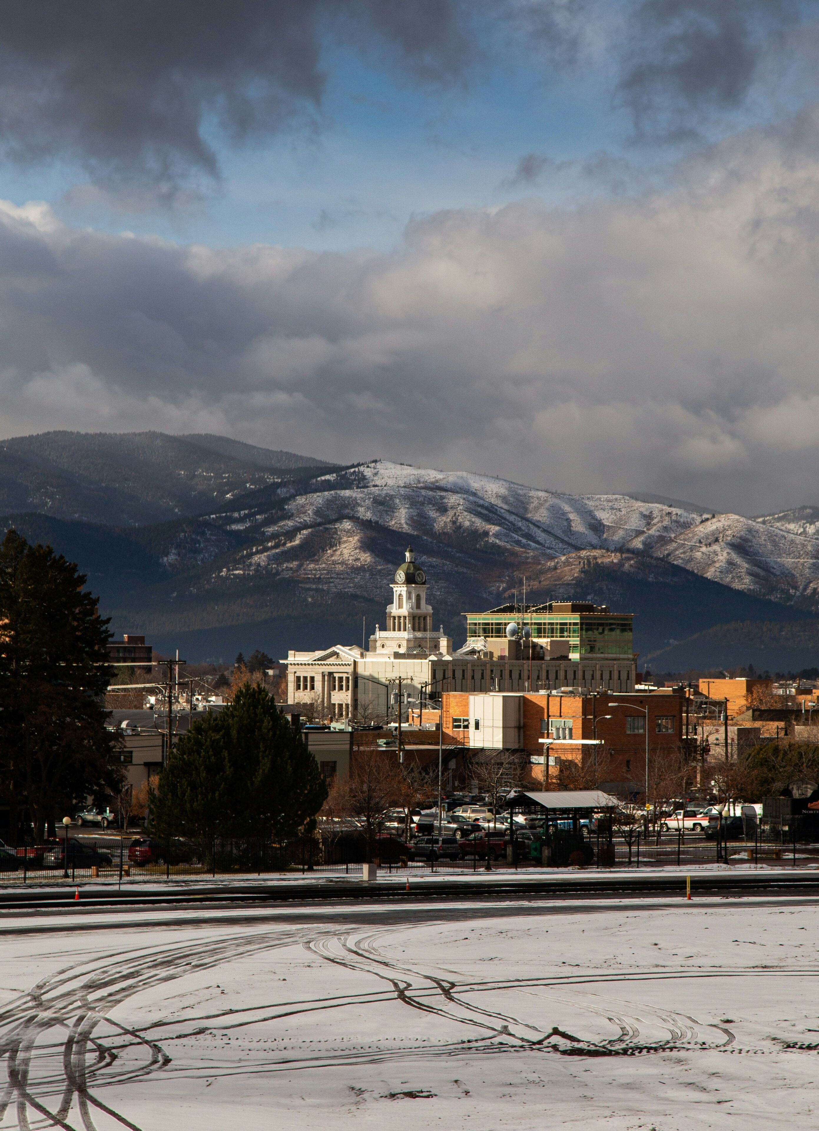 A town with a prominent clock tower, a snow-covered landscape, and mountains in the background.