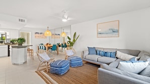 Ein modernes Wohnzimmer mit einer grauen Couch, blauen, gemusterten Hocker und einem Essbereich mit Holztischen und -stühlen.