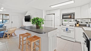 Eine moderne Küche mit weißen Schränken, einer zentralen Kochinsel mit Hockern, einer Mikrowelle, einem Herd und einem großen Fenster.