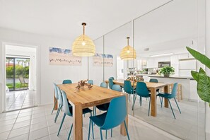 Un comedor moderno con una mesa de madera y sillas azules, una cocina al fondo y obras de arte en las paredes.