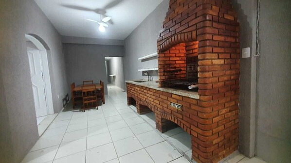 A room with a brick fireplace, a ceiling fan, a dining table with chairs, and a tiled floor.
