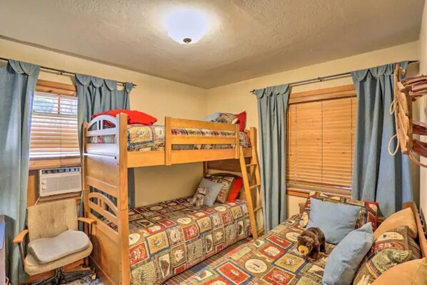 A bunk bed room with a desk and chair, a window with curtains, and a small dog.