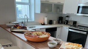 A modern kitchen with a wooden countertop, a large bowl of snacks, a plate of cheese and meats, and a coffee maker. - Lord & Patrick Condo at Bayfront Park (Miami)
