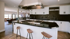 A modern kitchen with white cabinets, a black countertop, and a central island with bar stools. - Yount Ridge Estate, Yountville CA (Napa)