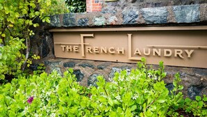 A sign for "The French Laundry" with a stone wall and greenery in the foreground. - Yount Ridge Estate, Yountville CA (Napa)