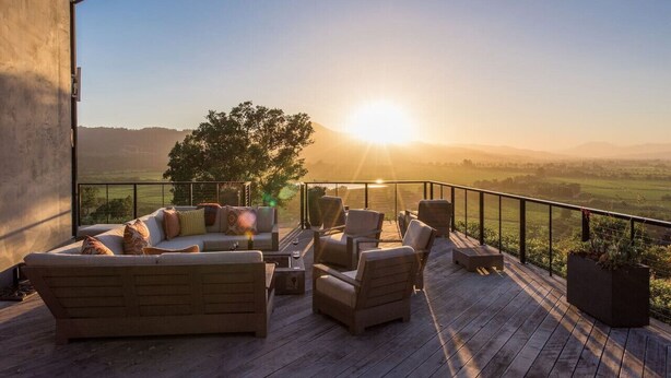 A deck with a sofa and chairs, overlooking a scenic landscape with a sunset. - Yount Ridge Estate, Yountville CA (Napa)