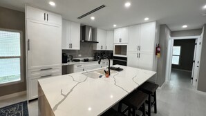 A modern kitchen with white cabinets, a large island, and a built-in oven. - Kaibo Kove (Rum Point)