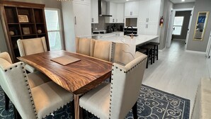 A modern kitchen with white cabinets, a central island, and a dining area with a wooden table and upholstered chairs. - Kaibo Kove (Rum Point)