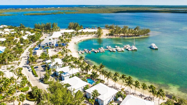 An aerial view of a coastal resort with multiple buildings, a marina with boats, and clear turquoise waters. - Kaibo Kove (Rum Point)