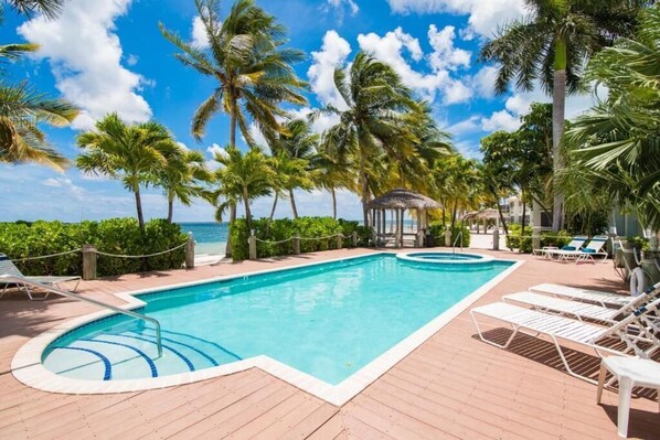 A pool area with lounge chairs, a gazebo, and palm trees.