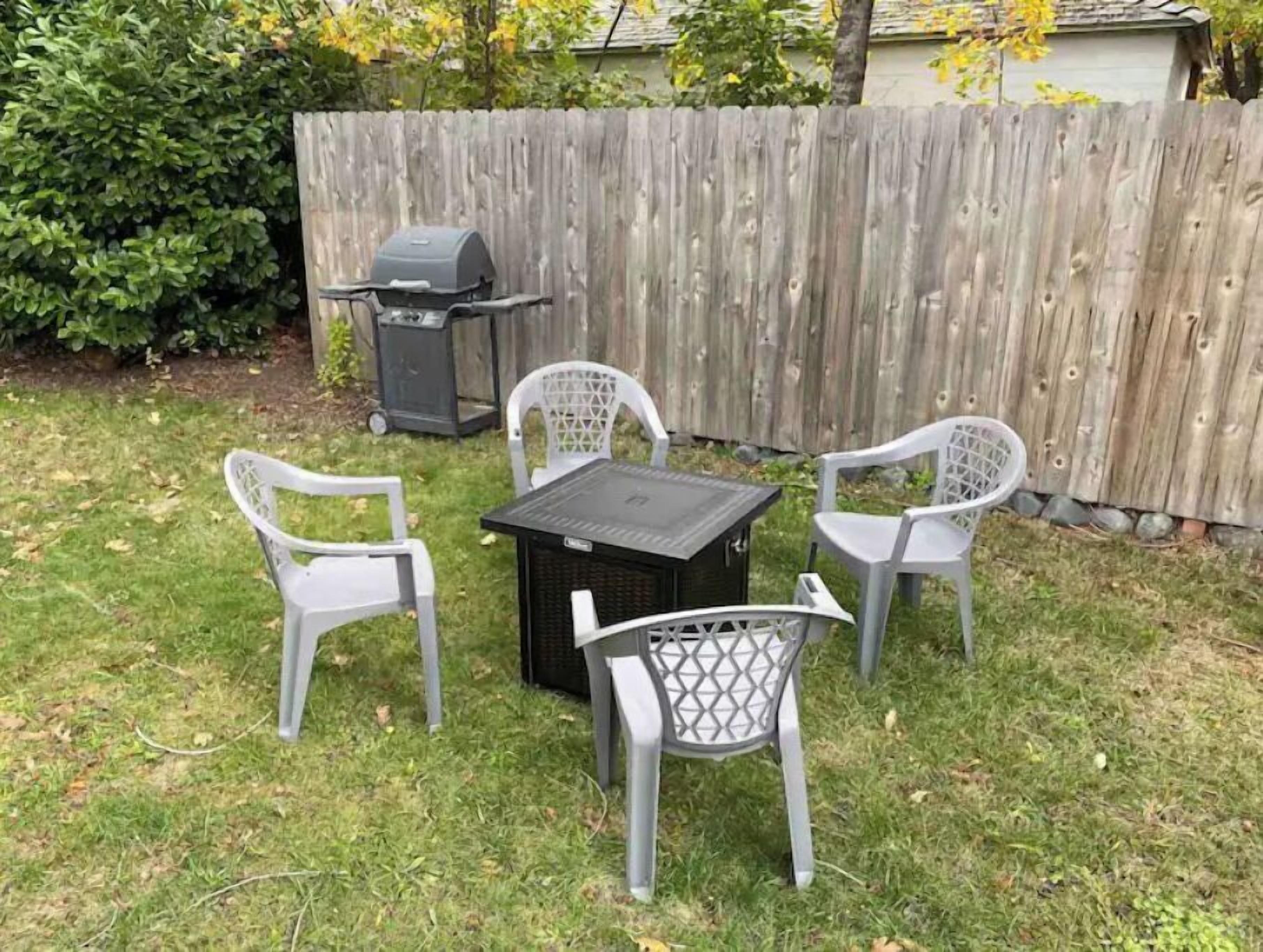 A backyard with a wooden fence, a grill, and a table with four chairs.