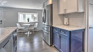 Una cocina moderna con un refrigerador de acero inoxidable grande, armarios blancos y un comedor con una mesa redonda y sillas.