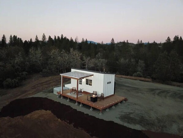 Situated in a natural setting, this cabin offers a covered patio with a wooden deck and outdoor seating.