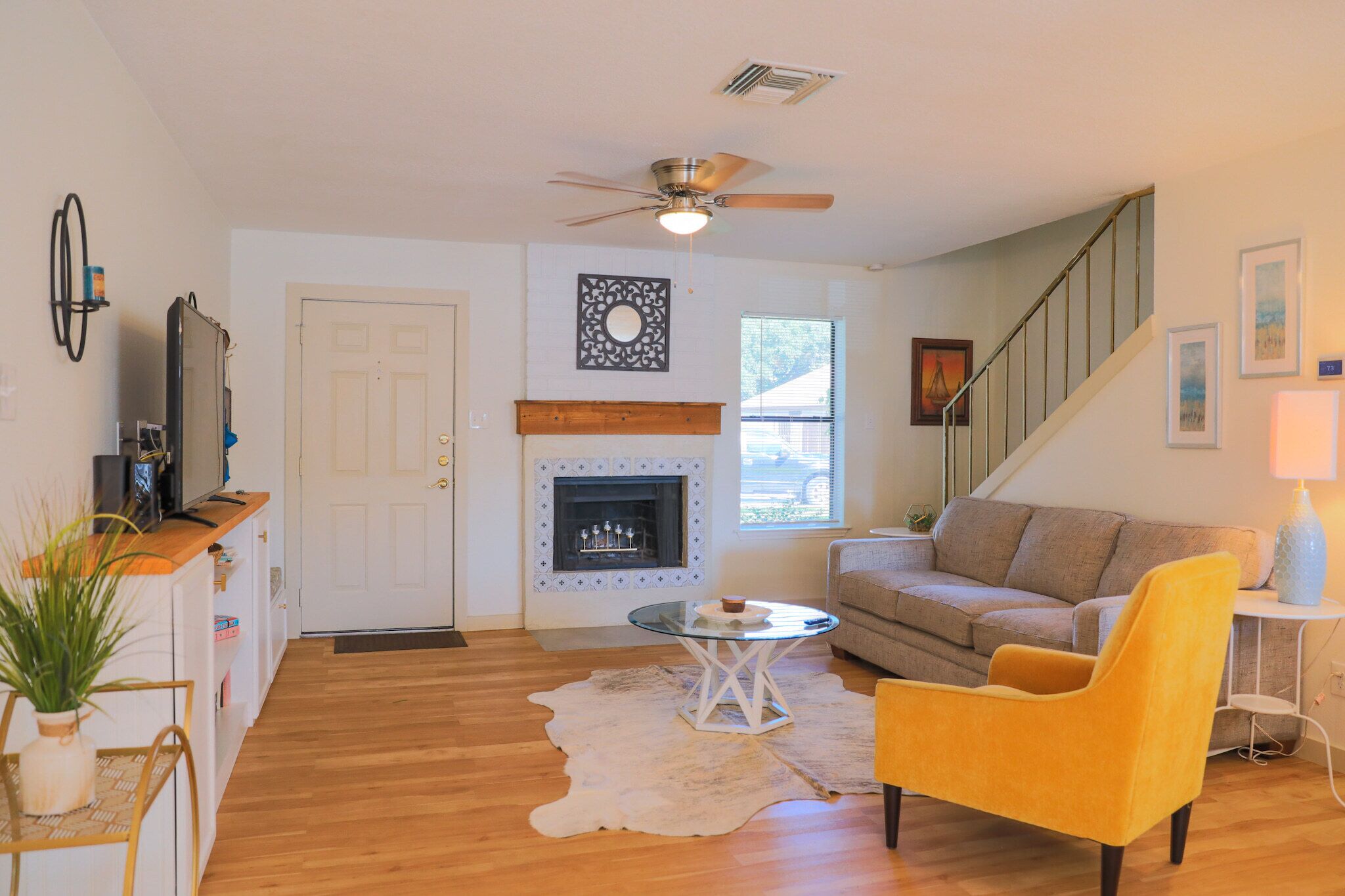 Una sala de estar con chimenea, un sofá, un sillón amarillo y una escalera.