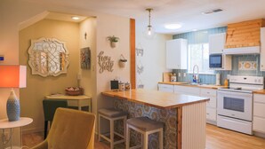 Une cuisine compacte dotée d’un îlot central, de meubles blancs et d’un plan de travail en bois.