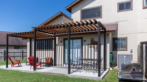 Un patio couvert avec des meubles d’extérieur, un barbecue et une vue sur une maison dotée d’un jardin clôturé.