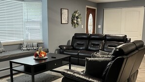 A living room with a black leather sofa, a coffee table, and a window with blinds.