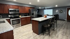 A modern kitchen with wooden cabinets, stainless steel appliances, a granite countertop, and a bar area with stools.