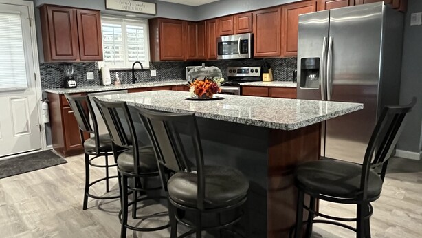 A modern kitchen with a central island, dark wooden cabinets, stainless steel appliances, and a granite countertop.